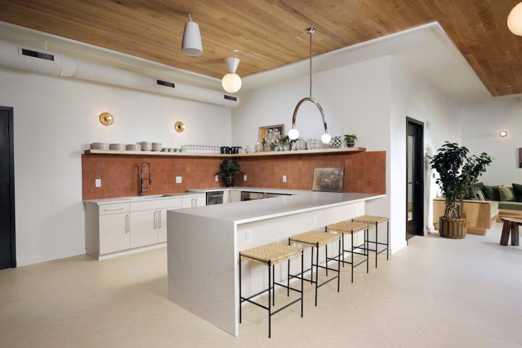 Kitchen with light-colored cabinets, a white quartz island with four stools, and a terracotta tile backsplash under an open shelf.