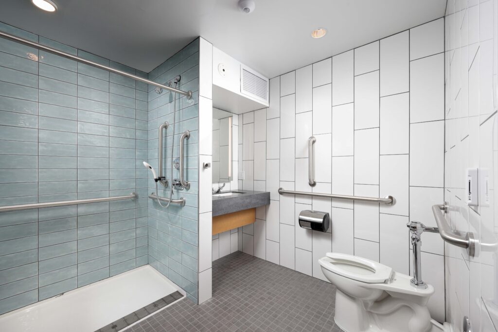 Accessible bathroom with a walk-in shower featuring blue tiles, a wall-mounted sink, and a toilet with grab bars.
