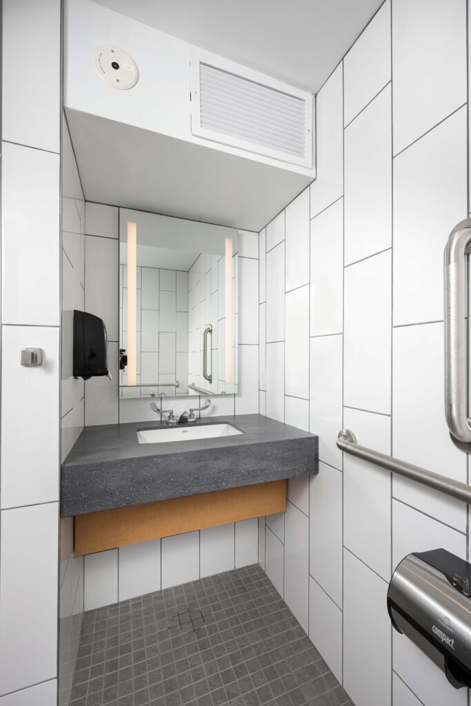 A bathroom sink with a wall-mounted mirror, white subway tile walls, and a metal grab bar.