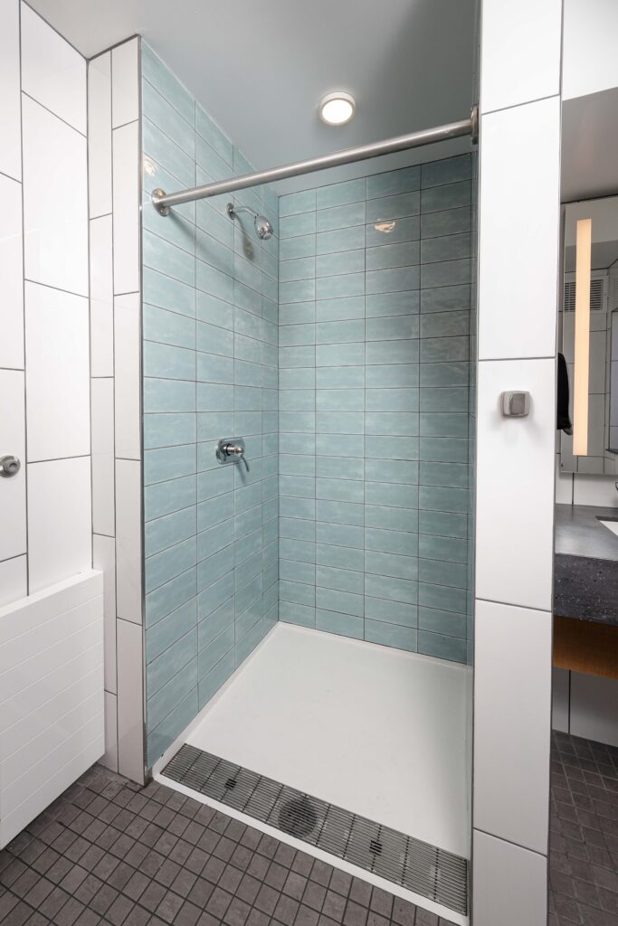 A shower stall with light blue subway tiles and a white floor, featuring a linear drain and a chrome shower head.