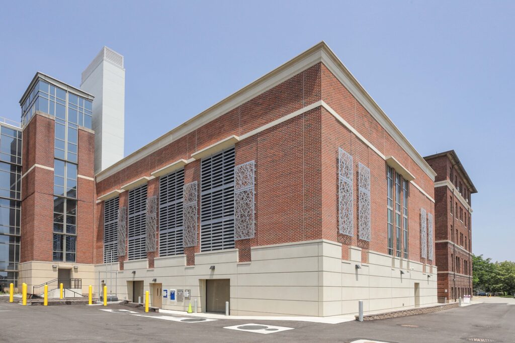 A brick building featuring a glass-enclosed stair tower and rectangular metal grill panels on the facade.