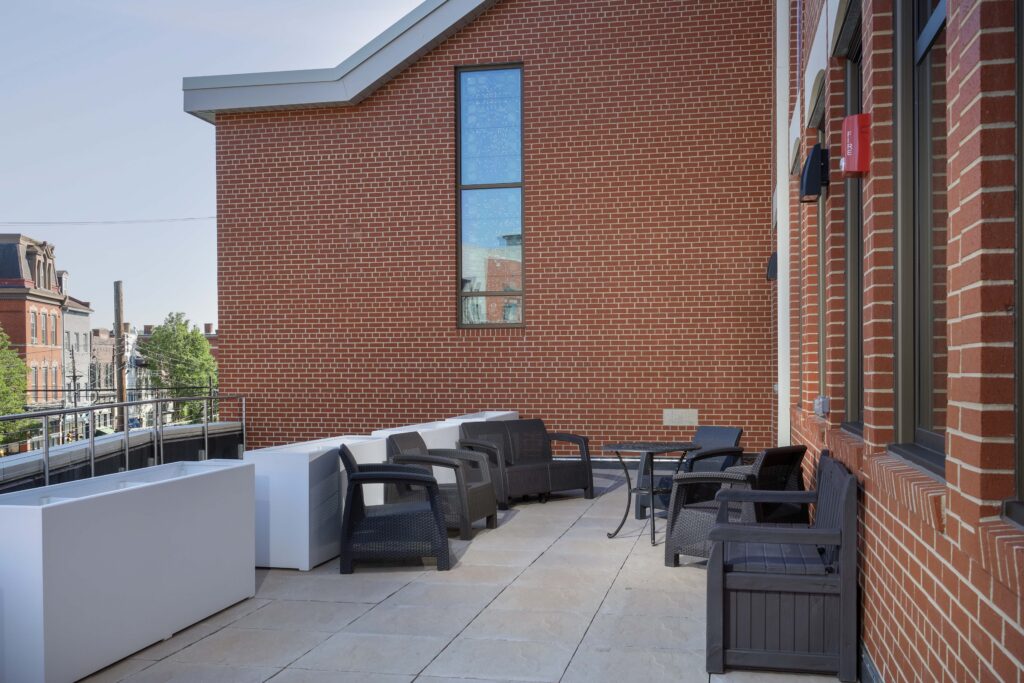 Rooftop patio with dark wicker outdoor furniture set against a red brick building wall.