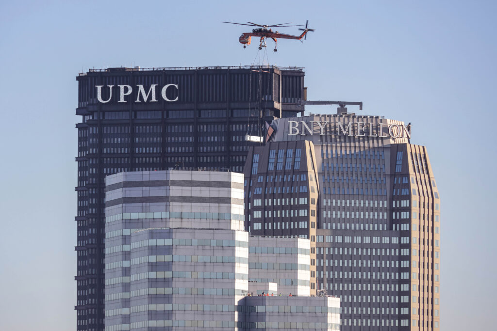 A helicopter lifting an object onto the roof of the UPMC skyscraper in Pittsburgh.