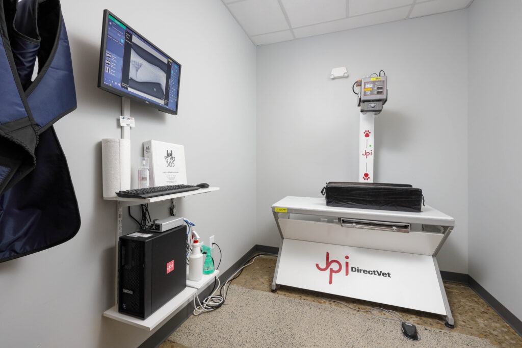 Veterinary X-ray station with a digital imaging table, monitor displaying a skeletal scan, and associated computer equipment.