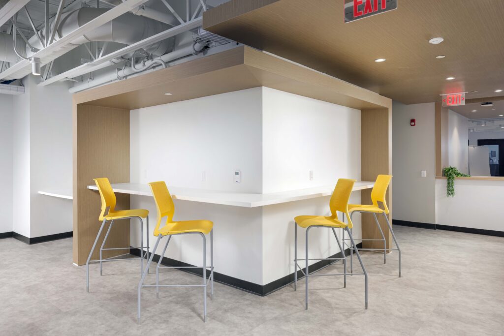 Four yellow bar stools at a white L-shaped corner desk in a modern office.