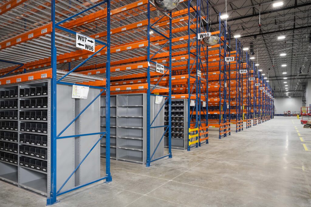Rows of tall blue and orange industrial warehouse shelving units with section labels like W06, W07, and W10.