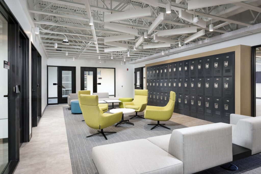 Office lounge area with chartreuse armchairs, grey modular seating, and a wall of grey metal lockers.