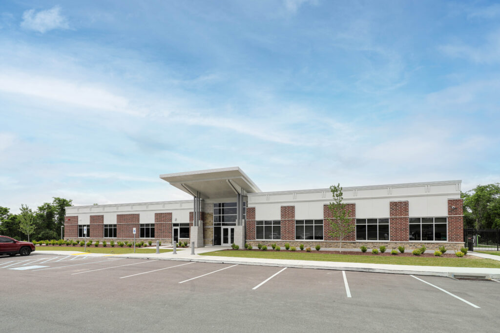 A low-rise commercial building with a brick and white panel facade, a prominent entryway canopy, and an expansive asphalt parking lot in the foreground.