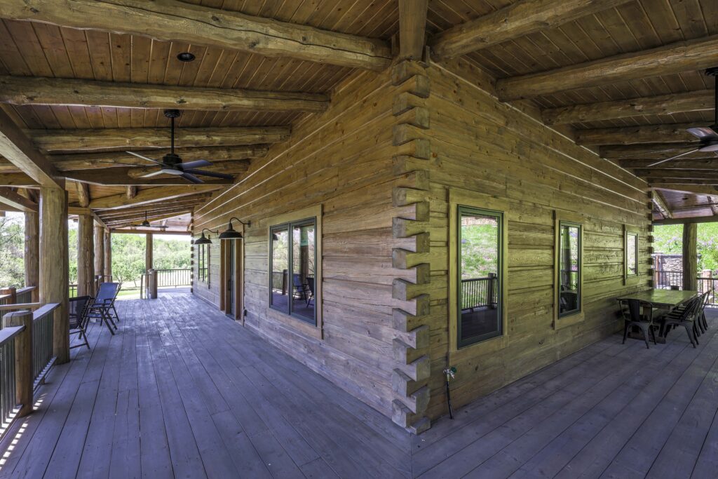 A wrap-around wooden porch on a log cabin with outdoor seating.