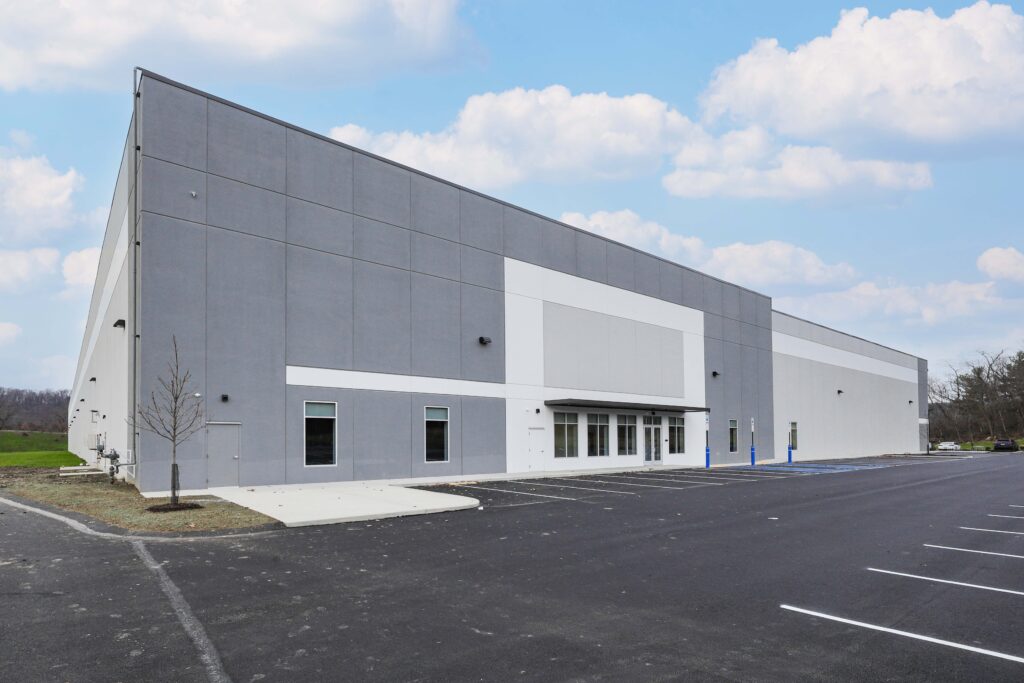 A large, modern grey and white warehouse building with an empty parking lot in the foreground.