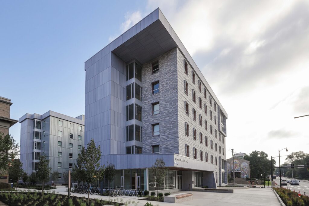 Modern multi-story dormitory building with grey metal and brick paneling on a university campus.