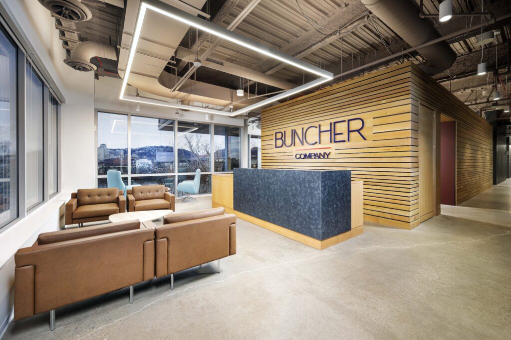 Reception area for The Buncher Company, featuring a front desk, lounge seating, and large windows with a view of the city.