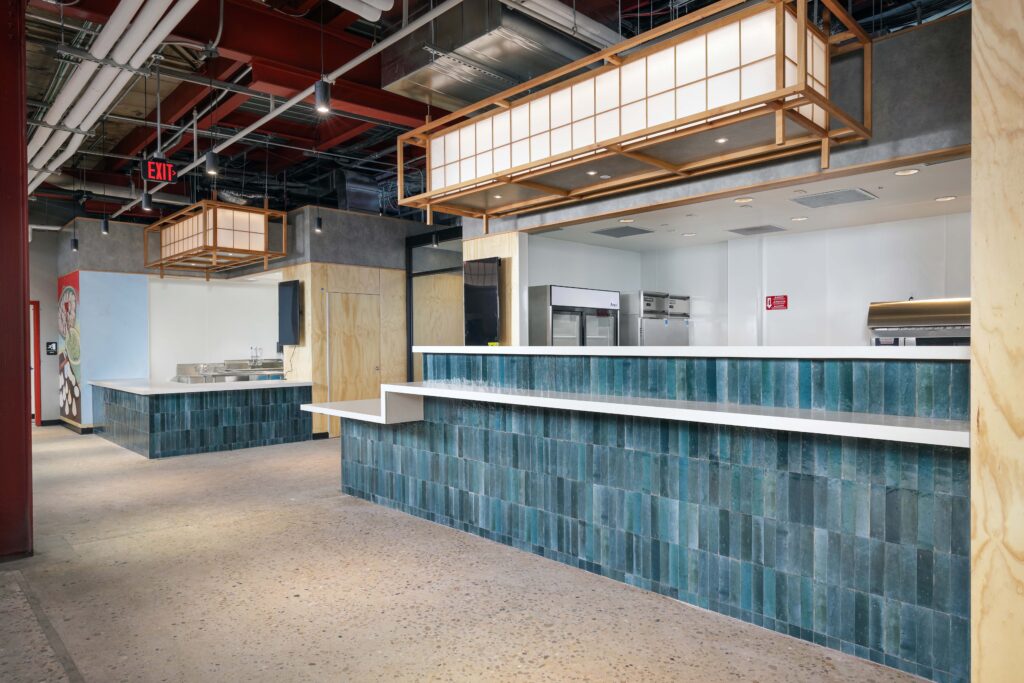 A restaurant service counter with blue-green tile, a white countertop, and Japanese-style lanterns hanging above.