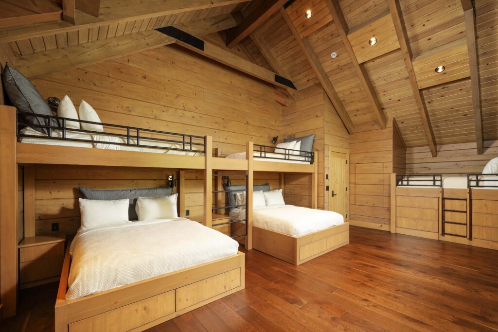 A rustic room with wood walls and vaulted ceiling featuring two sets of bunk beds with lower double beds.