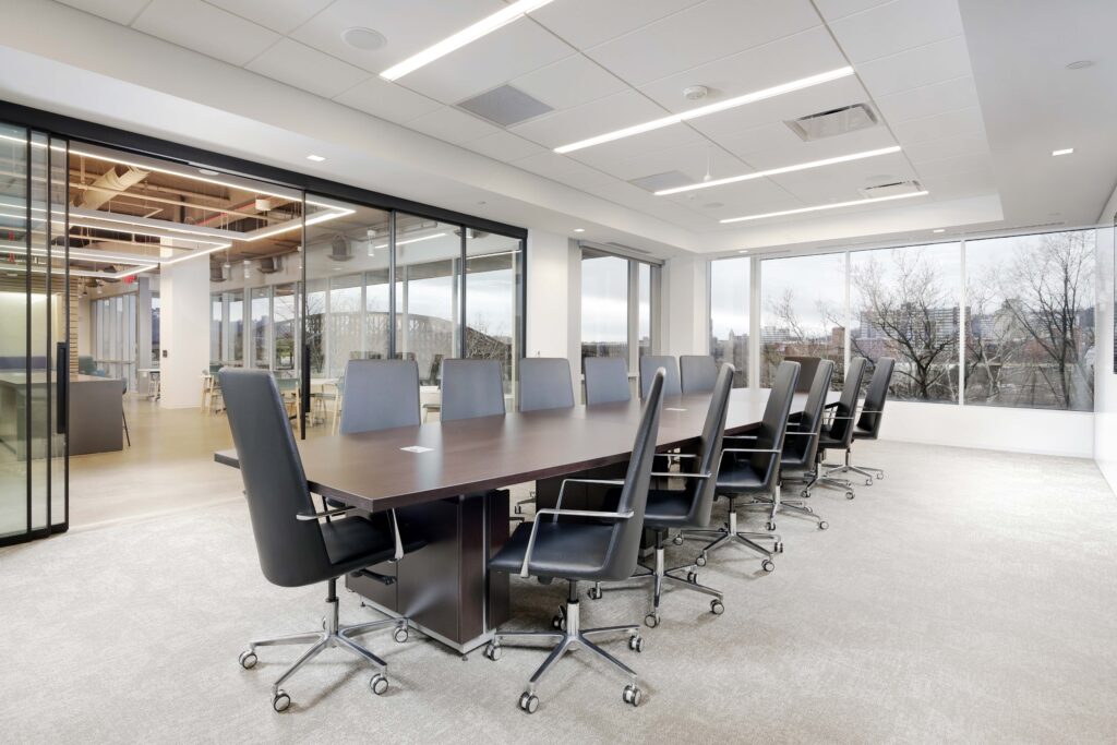 A long rectangular boardroom table surrounded by black office chairs in a modern office with floor-to-ceiling windows.
