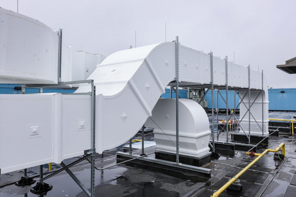 White industrial ductwork supported by metal framing on a flat rooftop.