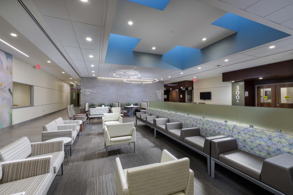 Modern waiting area with rows of upholstered armchairs, a long bench, and wayfinding signage for office suites.