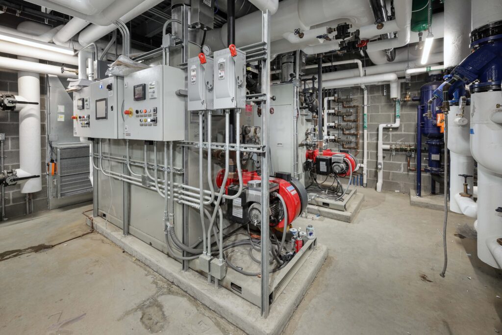 Mechanical room containing two industrial pump and control panel systems connected to overhead white piping.