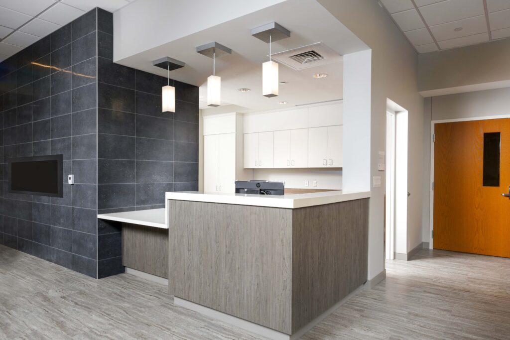 An office reception desk with a wood-look front, white countertop, and three pendant lights hanging above.