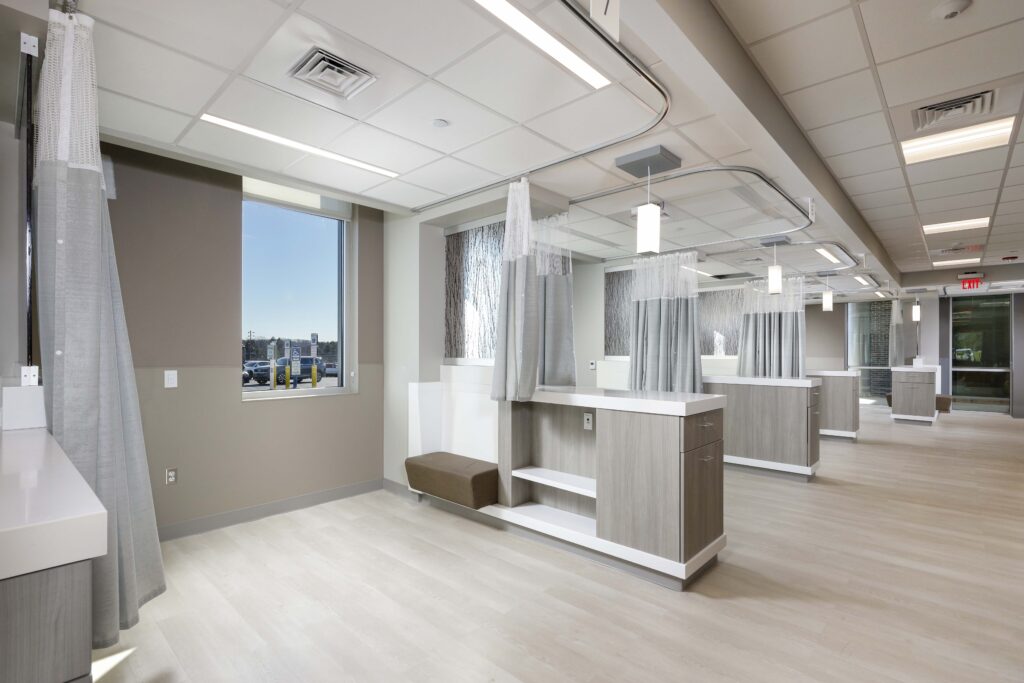 A modern medical exam room with multiple patient bays divided by privacy curtains and wooden cabinets.