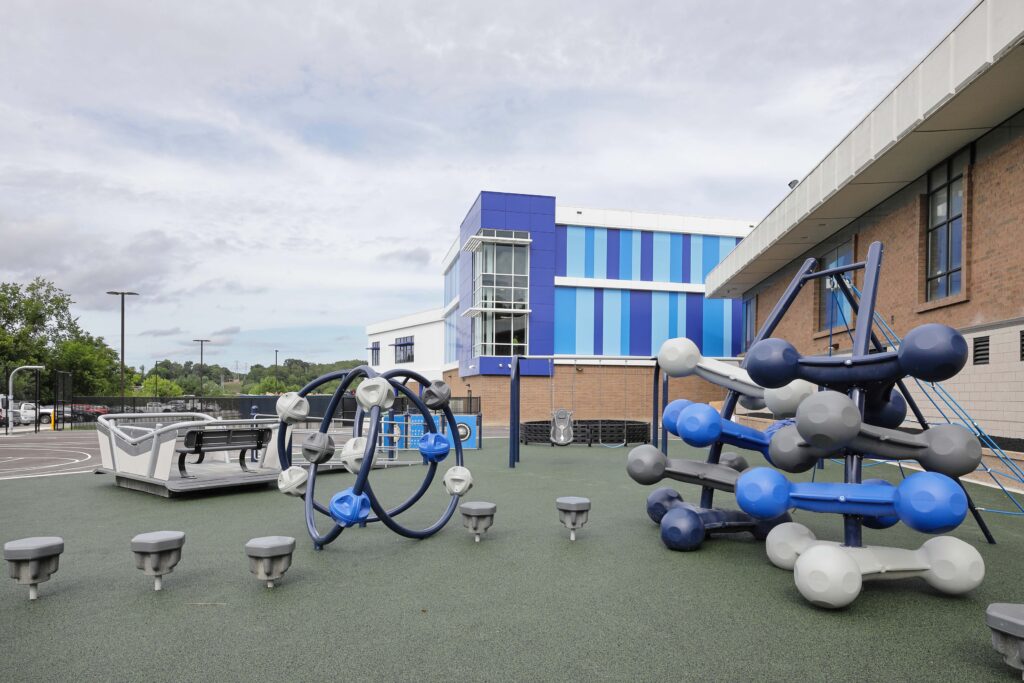 Modern playground with climbing structures and swings next to a blue and white school building.
