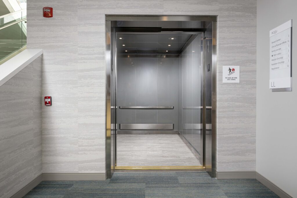 An open elevator door in a hospital hallway with a directory sign listing departments and a fire safety sign.