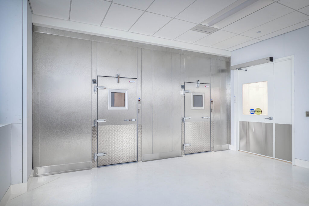 Two industrial stainless steel doors with small square windows and diamond-plate panels, next to a white door with a glass pane.
