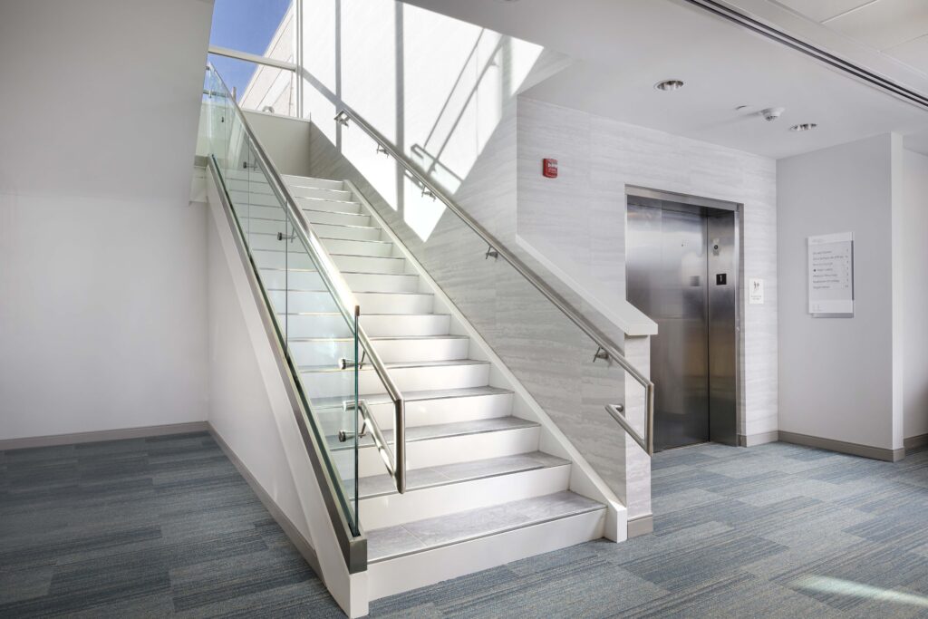 Staircase with glass railings next to an elevator and a building directory sign.
