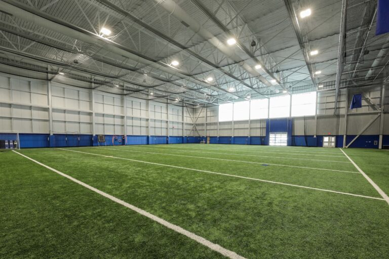 Indoor turf athletic field with white yard lines and high ceilings.