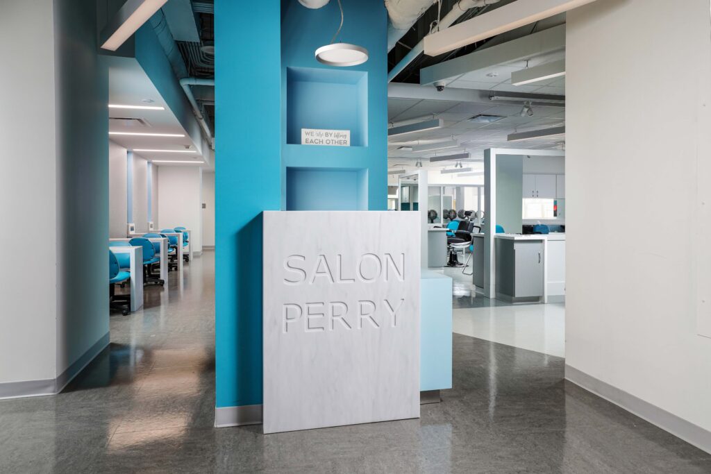 Reception desk with “SALON PERRY” embossed on the front, set against a bright blue wall in a hair salon interior.