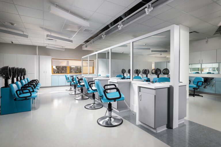 A hair salon training room with rows of blue chairs, mirrors, and hood dryers at stations.