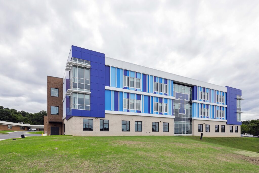 A three-story modern building with blue, light blue, and white geometric exterior paneling, partially constructed from tan brick.