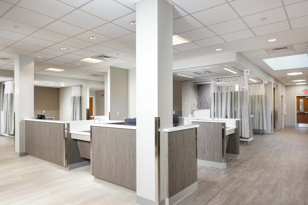 A clinical workspace featuring multiple patient care stations separated by privacy curtains, with wood-paneled counters and numbered signage.