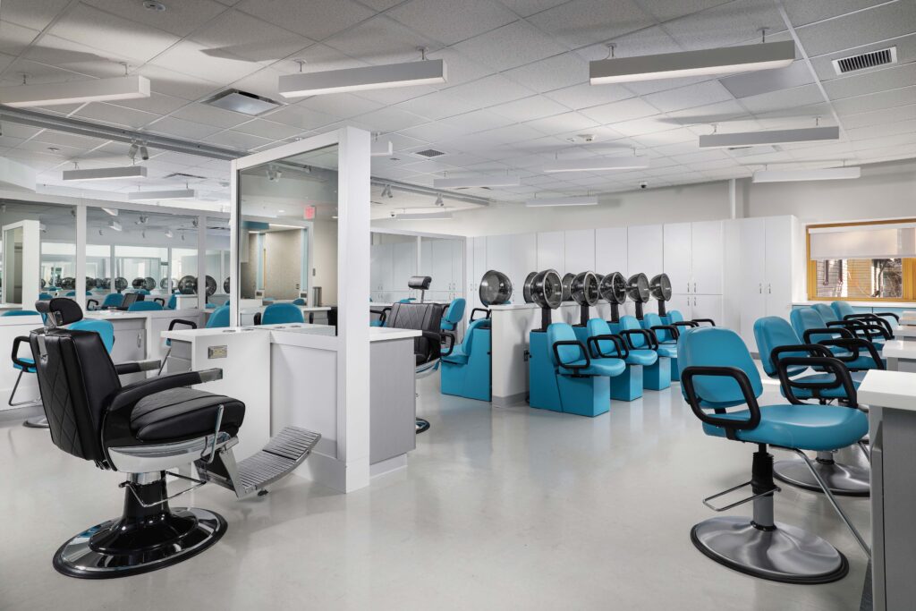 A hair salon with rows of blue styling chairs and black hooded hair dryers.