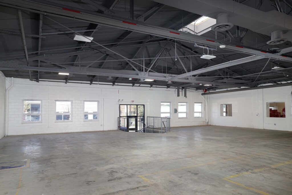 An empty, industrial-style room with white brick walls, a gray concrete floor, and an exposed ceiling structure with metal trusses.
