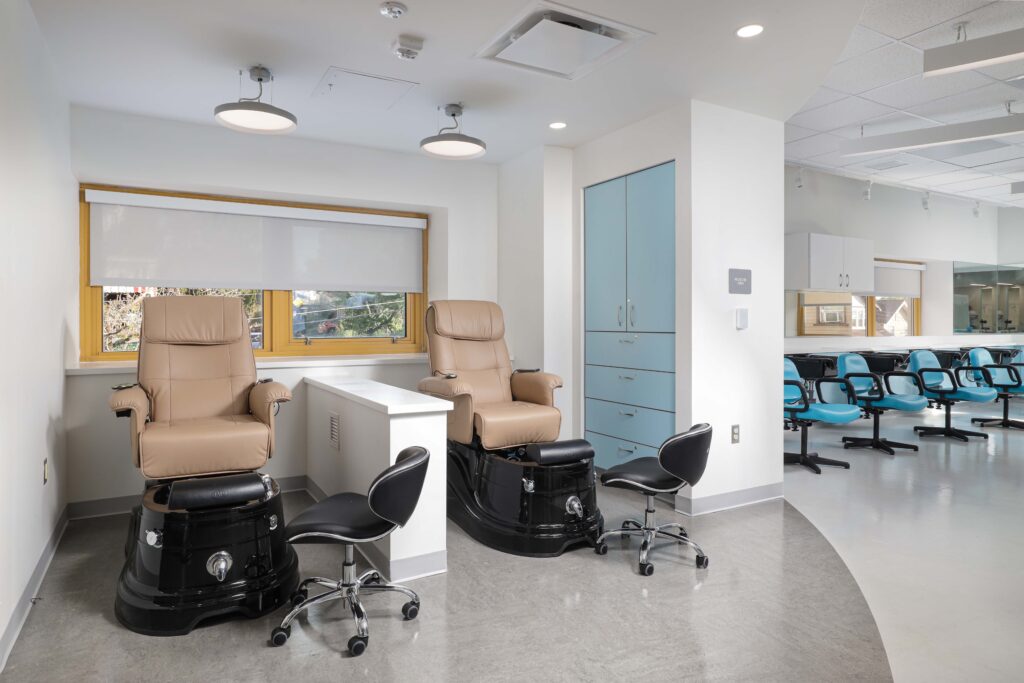 Two pedicure stations with tan chairs and black basins, featuring adjacent rolling stools in a bright, modern room.