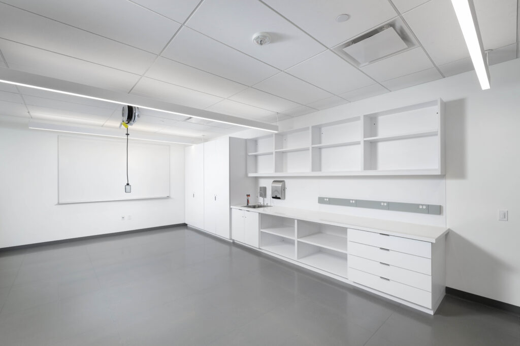 An empty laboratory with white cabinets, open shelving, a sink, and a whiteboard.