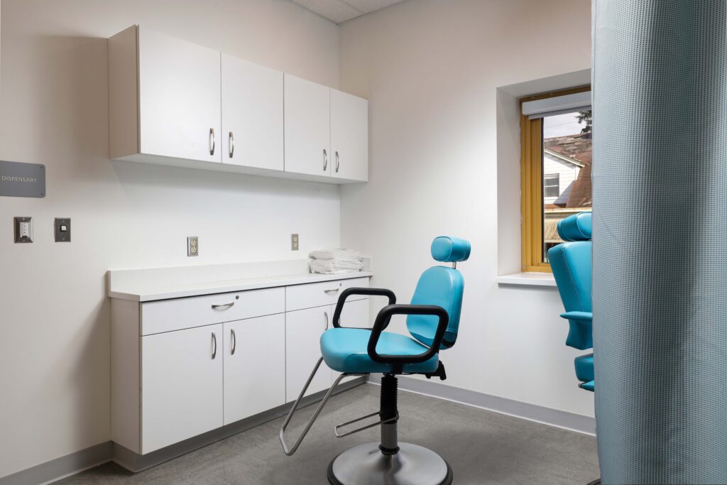 An examination room with white cabinetry and a blue dental chair.