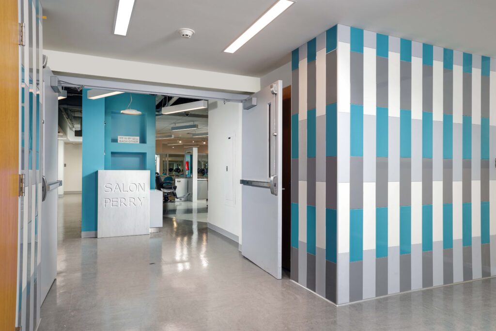 Entrance to Salon Perry, featuring a white reception desk and a pillar decorated with vertical teal, white, and grey tiles.