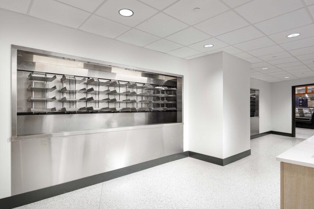 Stainless steel wall-mounted shelving unit with multiple divided compartments in an office kitchen or breakroom.