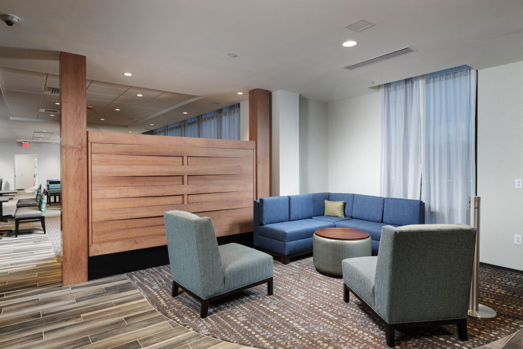 A lounge area with a blue sectional sofa, two armchairs, a round coffee table, and a wooden partition wall.