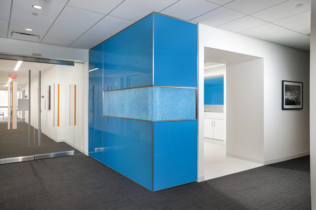 Modern office interior featuring a wall paneled in glossy blue glass with a central textured horizontal band.