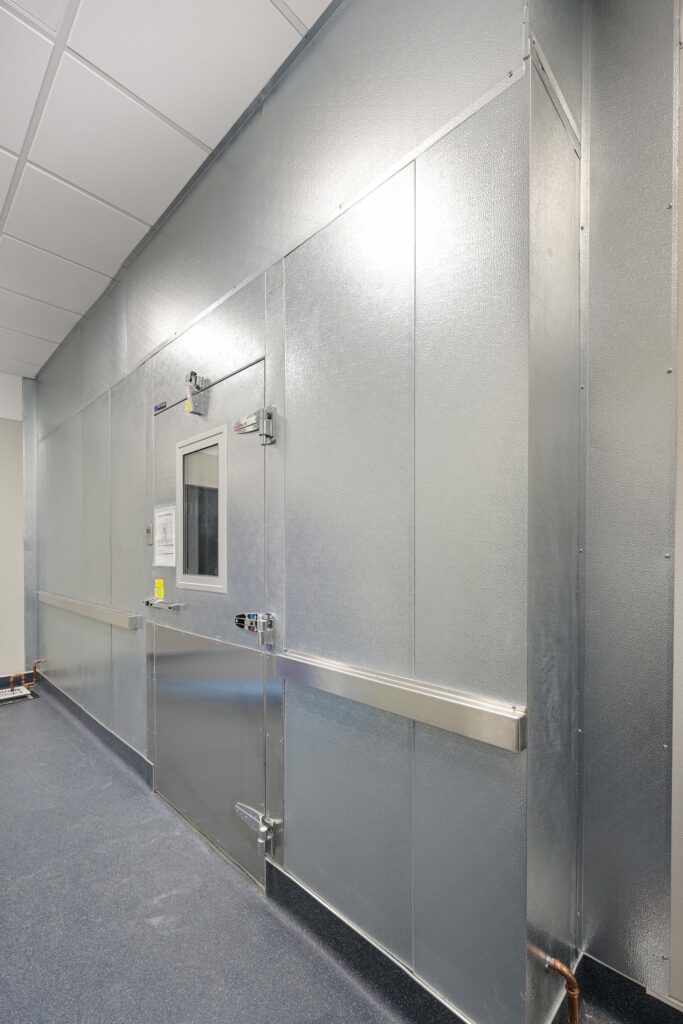 A stainless steel door with a viewing window set into a metal-paneled wall.