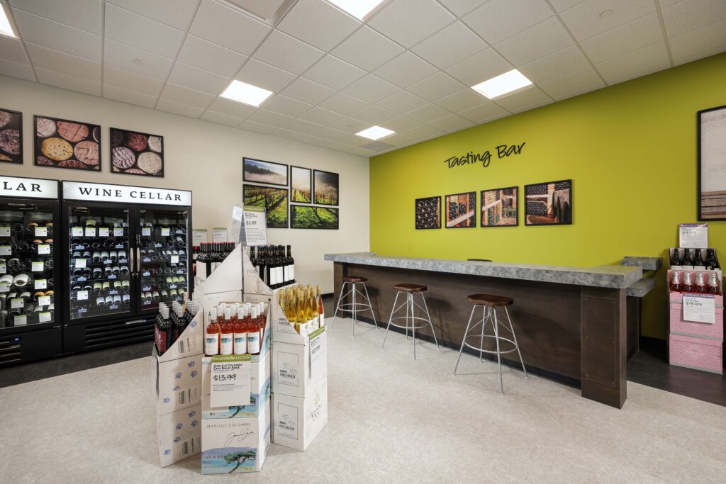 A wine cellar display featuring a refrigerated unit, cases of wine for sale, and a tasting bar with stools against a lime green wall.