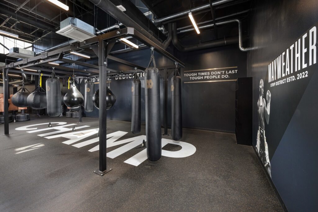 Boxing gym interior with a black punching bag rack and the word “CHAMP” printed on the floor.