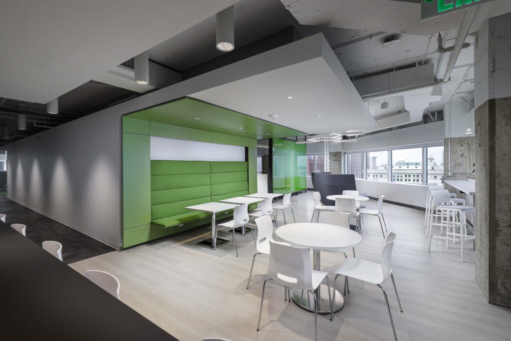 Modern office break room with white circular tables, chairs, and a long green built-in bench seating area.