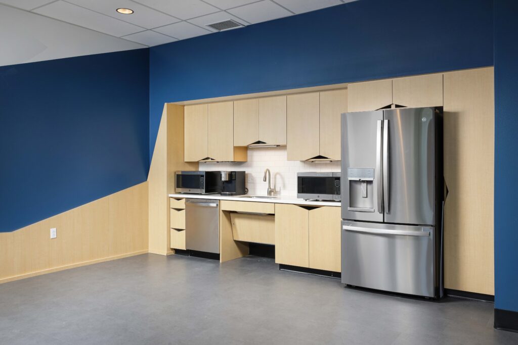 Office kitchenette with light wood cabinets, stainless steel appliances, and a blue accent wall.
