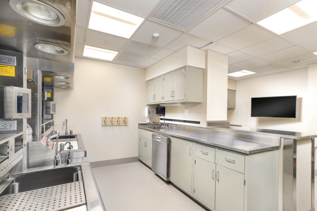 Commercial kitchen with stainless steel countertops, multiple sinks, a dishwasher, and a wall-mounted television.