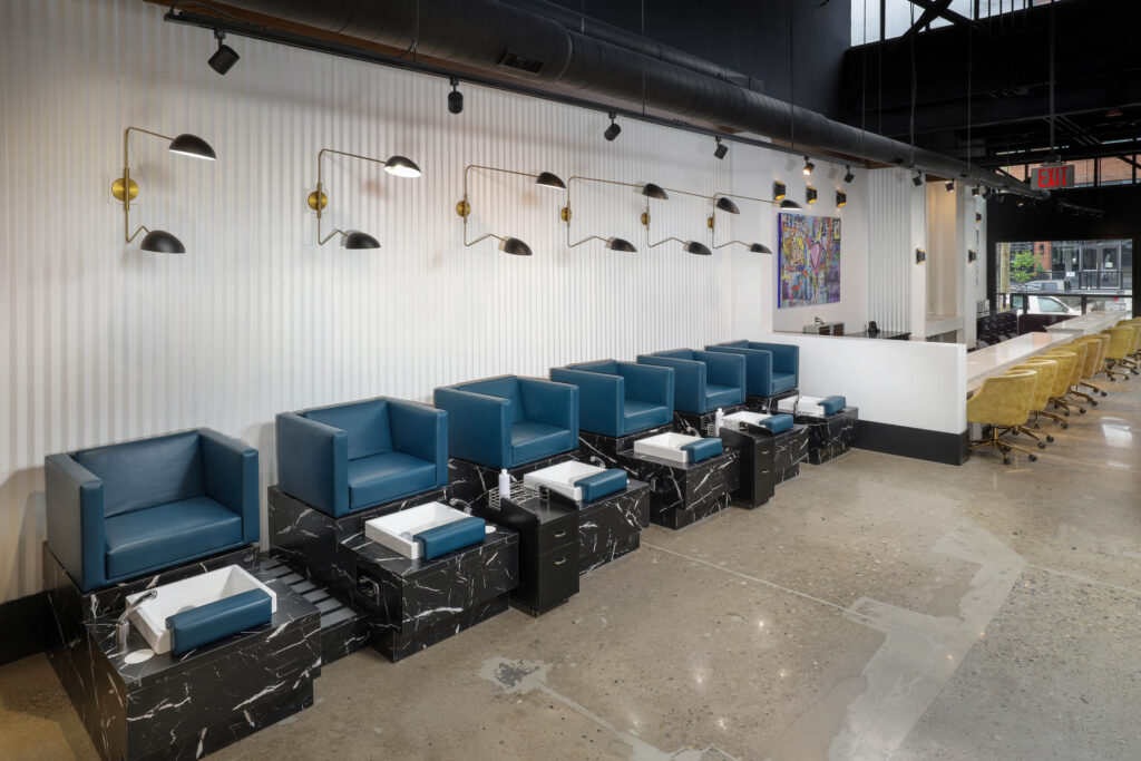A row of blue pedicure chairs with black marble bases and matching foot basins in a salon.