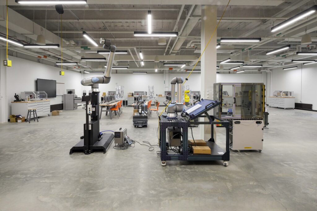 Two robotic arms in a brightly lit industrial laboratory space.